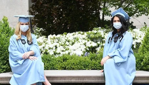 Two graduates masked and sitting distanced on a bench on morningside campus