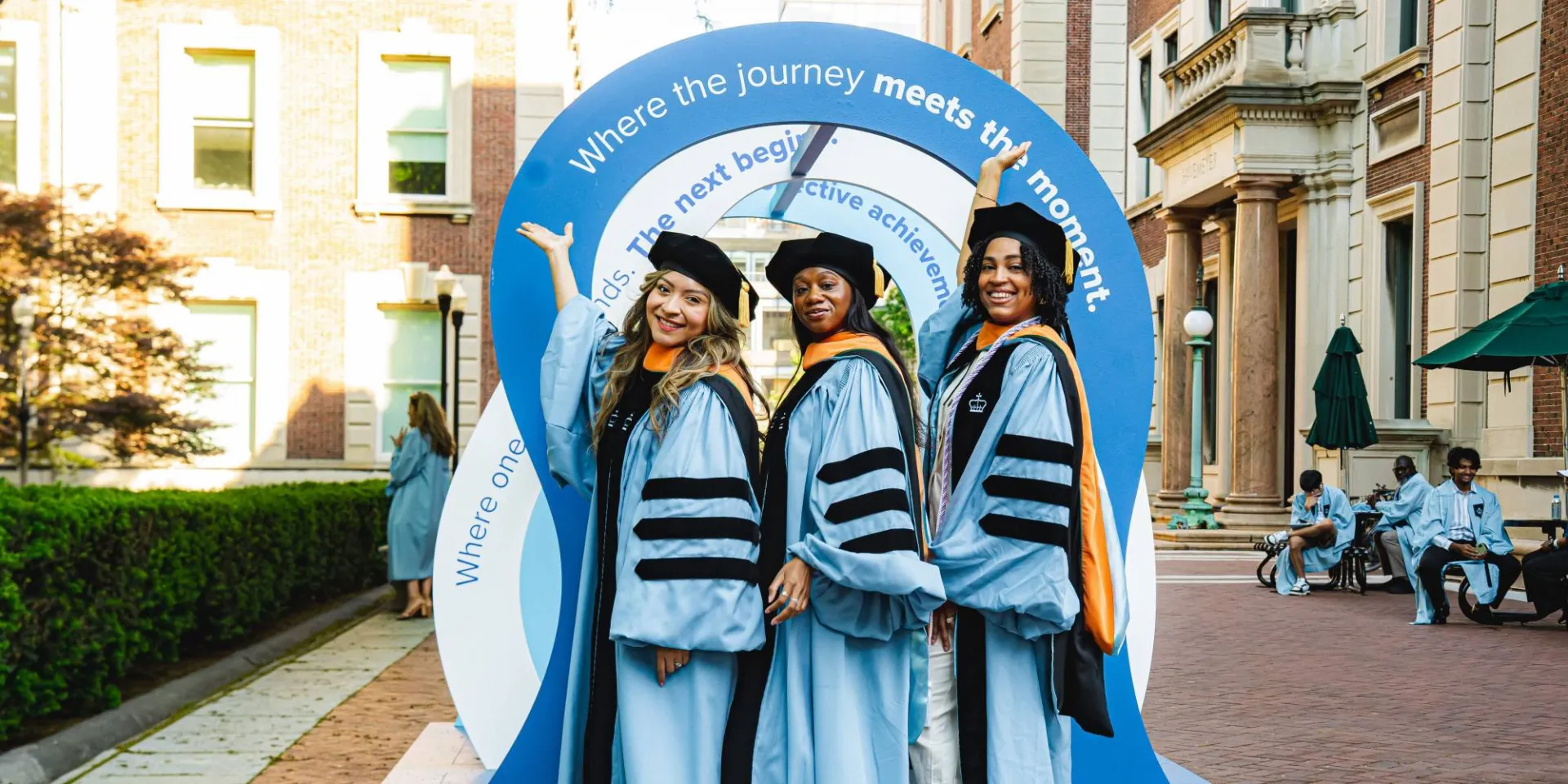 Graduates in front of a photo display on upper campus by Brandon Vallejo. 