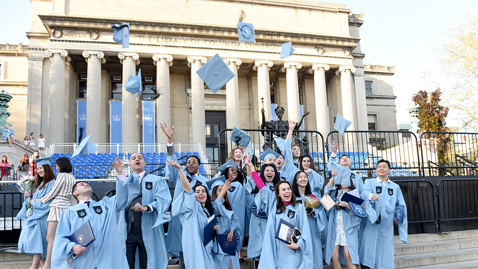 Columbian students celebrating University Commencement, throwing their caps into the air, in front of Alma Mater and Low Memorial Library.