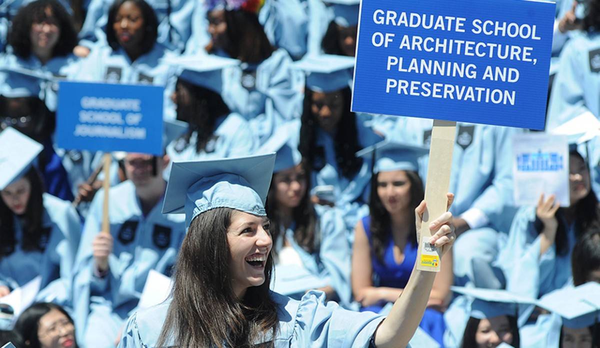Graduating student holding a “Graduate School of Architecture, Planning and Preservation” sign on Commencement Day